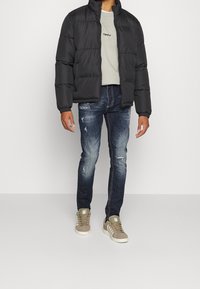 Musta toppatakki korkealla kauluksella, vaaleanharmaa T-paita, kuluneet siniset farkut ja vaaleanruskeat mokkanahkakengät valkoisilla pohjilla.