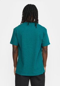 Teal katoenen T-shirt met korte mouwen en een relaxte pasvorm. Gladde textuur en ronde halslijn, met zijsplitten aan de onderrand.