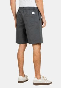 Graue Baumwollshorts mit einem elastischen Bund, zwei Gesäßtaschen und einem weißen Etikett. Gestylt mit weißen Turnschuhen.