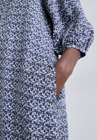 Rochie bleumarin dintr-un material texturat, cu un model abstract alb și albastru. Croi lejer, mâneci bufante și buzunare laterale.