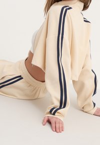 Conjunto de ropa cómoda de punto waffle en beige con rayas azul marino, que incluye una chaqueta corta con cremallera y pantalones cortos con cintura elástica para un ajuste cómodo.