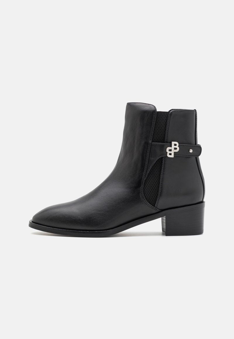 Bottine noire en cuir avec petit talon bloc, bout pointu, panneau latéral élastique et détail de boucle décorative argentée.