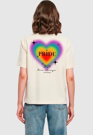 Cremfarbener Baumwoll-T-Shirt mit einer mehrfarbigen Herzgrafik, auf der "PRIDE 2024" und der Text "Liebe gewinnt immer" sowie Sterne Akzente zu sehen sind.