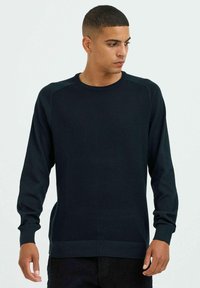 Pull en laine bleu marine avec des manches longues, des bords côtelés au niveau des poignets et de l'ourlet, et un panneau texturé sur le devant pour plus de détails.
