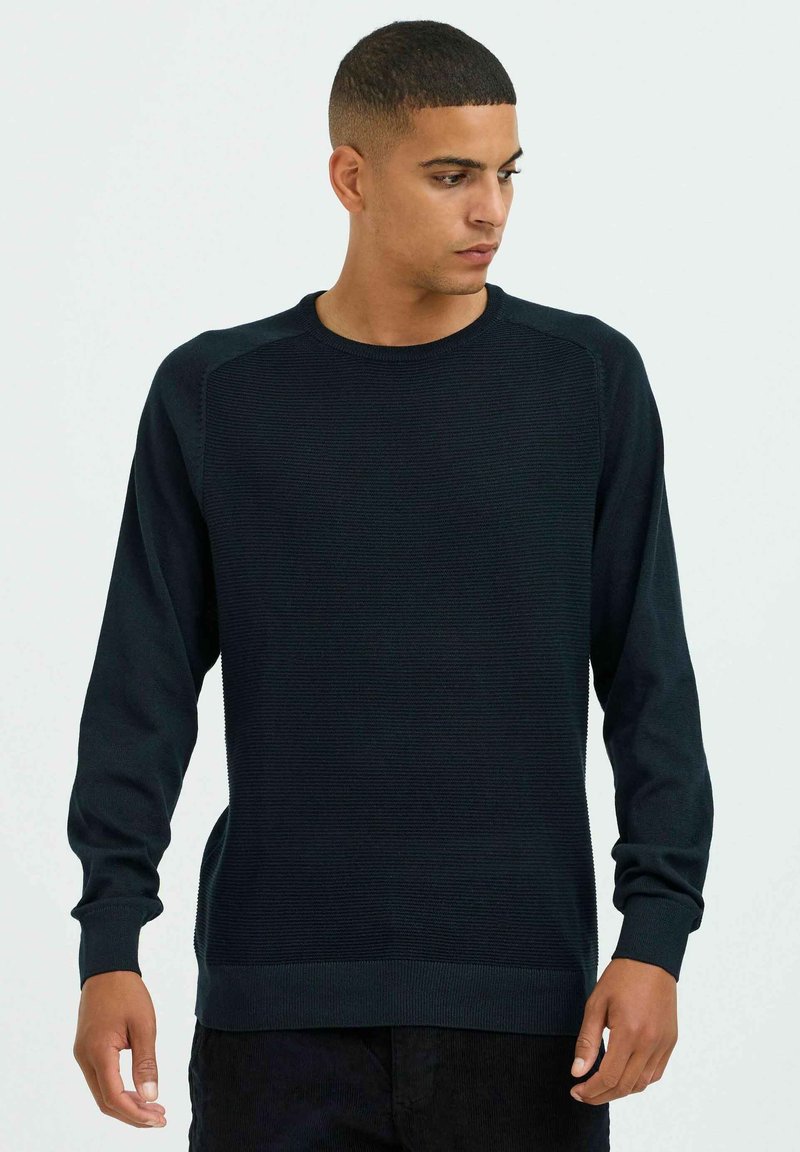 Pull en laine bleu marine avec des manches longues, des bords côtelés au niveau des poignets et de l'ourlet, et un panneau texturé sur le devant pour plus de détails.