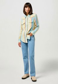 Πολύχρωμο πουκάμισο με κουμπιά, οριζόντιες ρίγες σε παστέλ αποχρώσεις, δύο τσέπες στο στήθος και κλασικό γιακά, σε συνδυασμό με ανοιχτό μπλε τζιν παντελόνι.