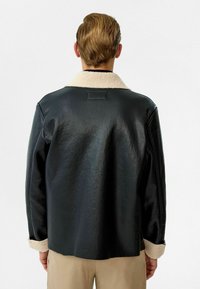Zwarte leren jas met een zachte beige shearling kraag en manchetten, met een gladde textuur en een eenvoudig, gestroomlijnd ontwerp.