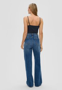 Jeans dżinsowe w kolorze niebieskim, o wysokim stanie i szerokich nogawkach, z gładką fakturą i dwoma tylnymi kieszeniami, noszone z czarnym topem na ramiączkach.