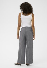 Široke sivo hlače izrađene od teksturirane tkanine s stražnjim džepovima i petljom za remen, uparene s bijelim topom bez rukava i crnim štiklama.