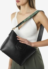 Zwarte leren schoudertas met een gestructureerde groene slangenpatroonriem. Voorzien van een magnetische flapsluiting en gouden hardware accenten.