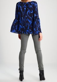 Námořnická modrá blůza s květinovým potiskem v modrých odstínech, s rukávy ve tvaru zvonu. V kombinaci s přiléhavými šedými kalhotami a černými kotníkovými botami.