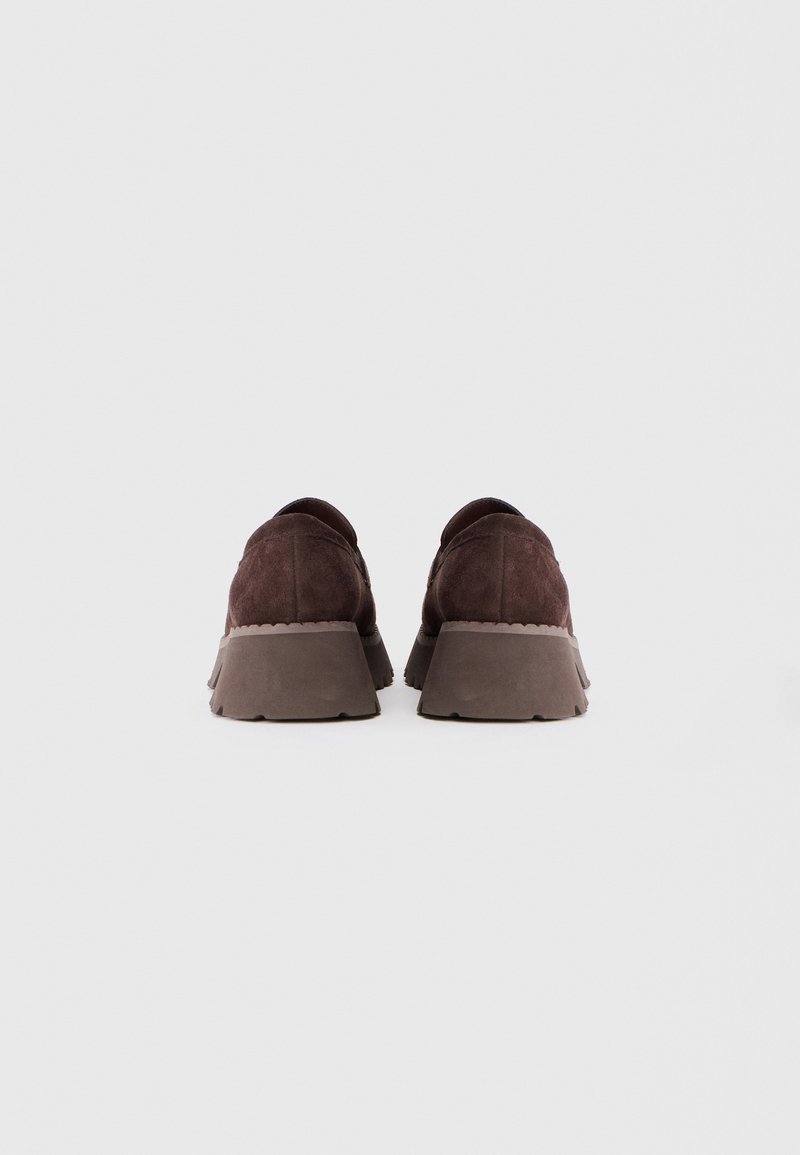 Scarpe platform in suede marrone viste da dietro su uno sfondo bianco con suole spesse e texturizzate.