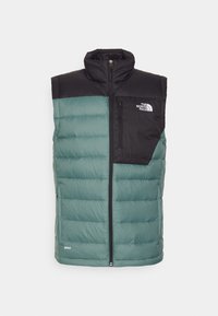 Gepolsterte Weste mit einem hellblauen unteren Bereich und einem schwarzen oberen Bereich. Verfügt über einen hohen Kragen, eine Reißverschlusstasche und ein Logo auf der Brust.