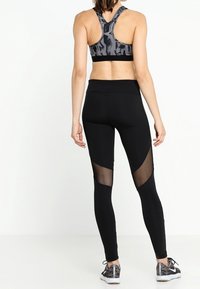 Leggings deportivos negros con recortes de malla y un sujetador deportivo con un patrón abstracto gris y diseño de espalda nadadora.