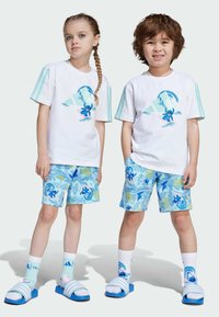 Två barn bär vita t-shirts med akvamarin detaljer, tryckta shorts med en tecknad karaktär och blå sandaler med vita ränder.