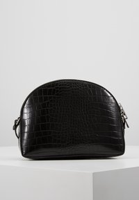 Borsa nera in ecopelle di cocodrillo con forma arrotondata. Dotata di chiusura con zip e accenti in metallo. Texture liscia con motivo impresso.