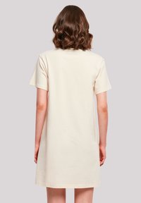 Kurzärmliges, cremefarbenes Baumwoll-T-Shirt-Kleid mit geradem Schnitt und dezenter Struktur, das in der Rückansicht bis zur Mitte des Oberschenkels reicht.