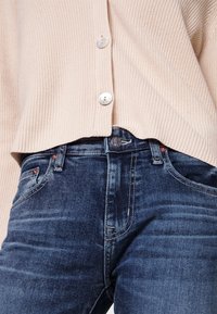 Ljusrosa ribbad cardigan med tre stora knappar, matchad med mörkblå denimjeans som har subtila nötningsmärken och klassisk fem-fickors stil.