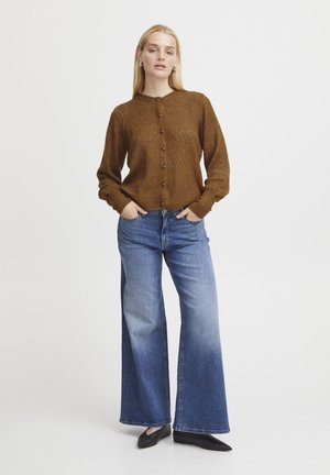 Brun stickad cardigan med ett diamantmönster, knäppning fram, och långa ärmar, tillsammans med vida blå jeans och svarta lägenheter.