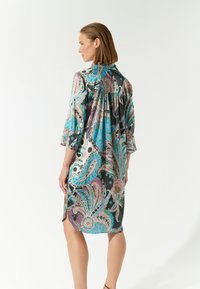 Fließendes Kleid mit einem lebhaften Paisleymuster in Türkis, Pink und Schwarz. Es hat Dreiviertelärmel und eine lockere Passform.