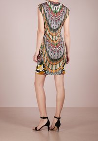 Barevné bezrukávové šaty s geometrickým vzorem v červené, zelené, žluté a černé; doplněné černými lodičkami s řemínkem kolem kotníku.