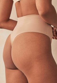 Keha poolt kõrgel asetsev nude värvi aluspüks, valmistatud siledast ja venivast kangast. Omab ühtegi õmblust mitte sisaldavat disaini ning pehmet tekstuuri, rõhutades vööd ja puusasid.