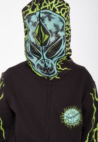 Haut à capuche noir avec un graphique d'aliens verts sur la capuche, des accents vert clair et un logo sur la poitrine. Tissu doux, fermeture éclair.