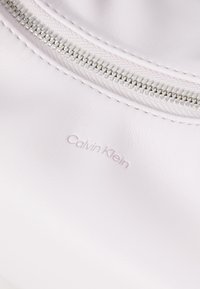Calvin Klein branded light pink leather with a smooth texture, featuring a silver zipper and subtle embossed logo detail.