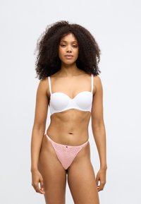 Soutien-gorge rembourré blanc avec fines bretelles associé à un string en dentelle rose avec broderies florales. Texture lisse avec des détails complexes.