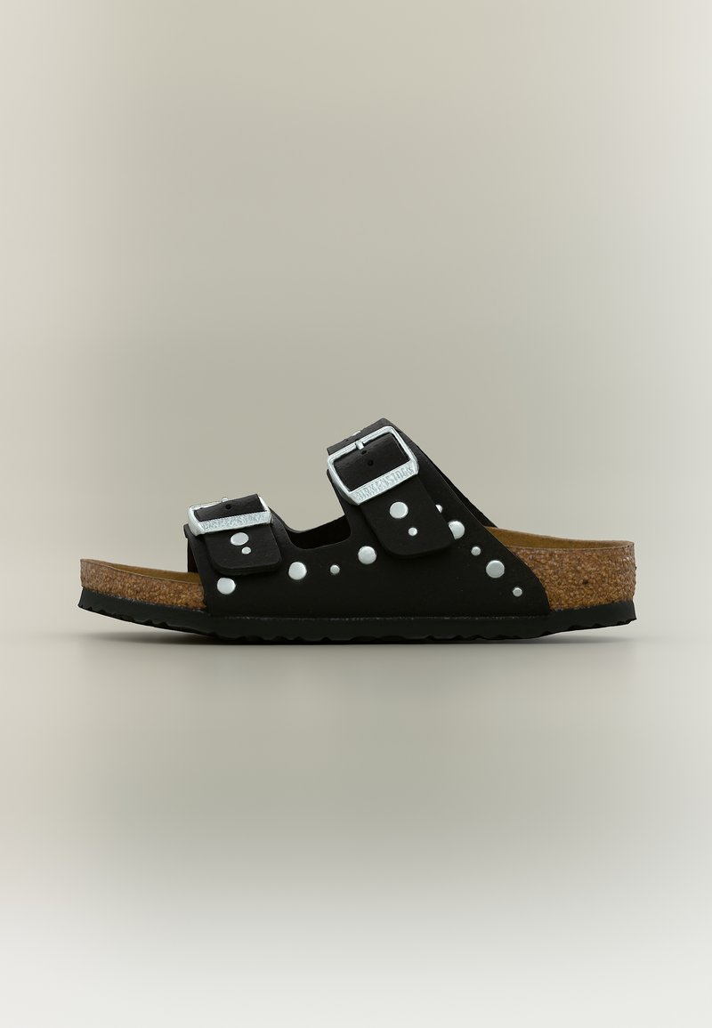 Μαύρο σανδάλι με ανοιχτά δάχτυλα, σόλα από φελλό, δύο ρυθμιζόμενες ασημένιες αγκράφες και λευκό πουά σχέδιο στα λουριά, εμφανιζόμενο από το πλάι.