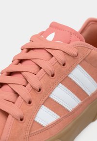 Ροζ σουέτ αθλητικό παπούτσι με λευκές δερμάτινες ρίγες, με ταιριαστά κορδόνια και λαστιχένια σόλα. Μαλακή υφή με λογότυπο στη γλώσσα.