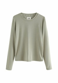 Lys oliven langærmet crew neck skjorte med et "self." mærke indeni kraven, præsenteret mod en hvid baggrund.
