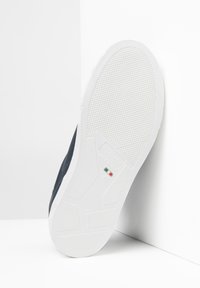 Sneaker navy con suola in gomma bianca. Presenta un motivo di grip testurizzato e dettagli di branding, esposto da un'angolazione su uno sfondo bianco.
