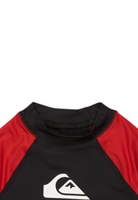 Krátky rukáv rash guard vyrobený z elastického čierneho a červeného materiálu, s bielym logom na prednej strane a vysokým golierom.