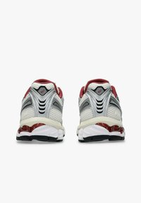 Un paio di scarpe da corsa bianche e grigie con accenti rossi, viste da dietro su uno sfondo bianco.