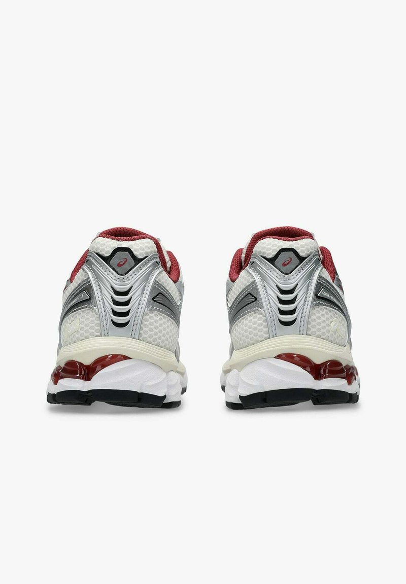 Un paio di scarpe da corsa bianche e grigie con accenti rossi, viste da dietro su uno sfondo bianco.