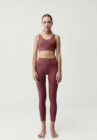 Burgundský sportovní podprsenka a legíny vysokého pasu vyrobené z hladkého, elastického materiálu. Obsahují švy a těsný střih.