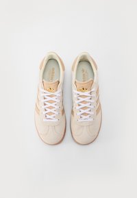 Ljusbeige sportskor med ovandel i mocka, vita snören och tre tonala ränder. Med en slät gummisula och detaljer i guldlogotyp.