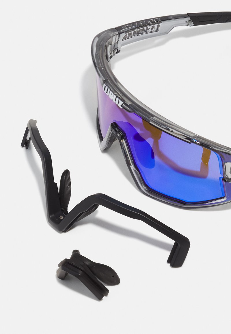 Sportliche Sonnenbrille mit transparentem grauen Rahmen und blauen Verlaufslinsen. Enthält abnehmbare schwarze Komponenten für eine anpassbare Passform.