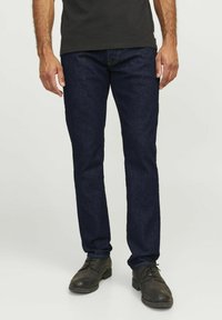 Dunkelblaue Denim-Jeans im Slim-Fit, ausgestattet mit einem klassischen Fünf-Taschen-Design und genähten Details, kombiniert mit schwarzen Dressschuhen.
