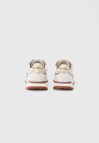Een paar witte en bruine sneakers met gouden accenten en "KARL LAGERFELD"-branding op de hiel, gezien van achteren tegen een effen achtergrond.
