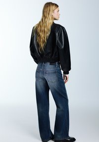 Crna kožna bomber jakna s rebrastim manšetama, uparena s trapericama visokog struka širokih nogavica plave boje. Glatka tekstura, jedinstvene dizajnerske značajke.