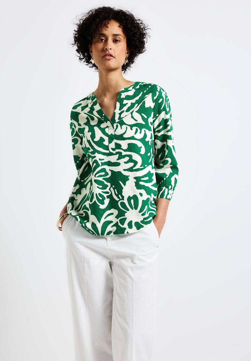 Camisa de lino a rayas verdes y blancas con medio placket y mangas de tres cuartos, combinada con pantalones anchos de color claro.