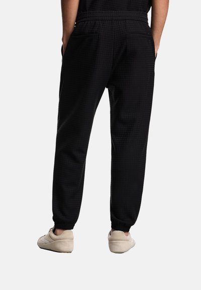 Pantaloni da jogging neri con un motivo testurizzato, vita elasticizzata, tasche laterali e aperture delle gambe affusolate, abbinati a calzature beige.