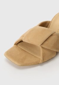 Sandal cu vârf pătrat din suede bej, cu un design larg cu curea încrucișată și o talpă netedă și texturată.