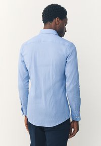 Camicia a righe azzurre a maniche lunghe con colletto a punta e polsini con bottoni, caratterizzata da una vestibilità sagomata e orlo curvo.