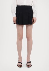 Musta pleated-minihame, joka on valmistettu sileästä kankaasta, jossa on korkea vyötärö ja sivusaumapokkereita. Yhdistetty mustiin remmisandaaleihin.