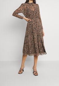 Braun und schwarz gemustertes Midi-Kleid mit langen Ärmeln, tailliertem Bund und ausgestelltem Rock, kombiniert mit schwarzen Riemchenschuhen.