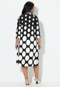 Svartvitt prickigt klänning med trekvartärmar, en krage med ett litet mönster och en flödande silhuett, i kombination med vita klackar.