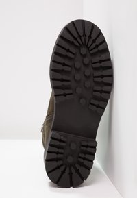 Botte en suède marron avec une semelle extérieure en caoutchouc noir robuste présentant des motifs hexagonaux et striés pour une meilleure traction. Détail de fermeture éclair sur le côté.
